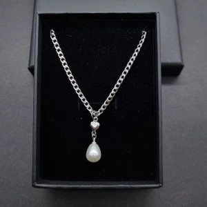 Silverhalsband med hjärta och pärla - Stilrent halsband i silverfärgad kedja med ett litet hjärta och en droppformad vit pärla som hänge. Material-rostfritt stål 
