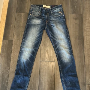 Replay Anbass jeans blå slim fit - Snygga Replay Anbass jeans i mörkblå tvätt med slitningar och skinny fit. Klassisk femficksmodell med orange sömmar och Replay-logga vid bakfickan. Jeansen har dragkedjegylf och är tillverkade i stretchig denim för extra komfort.