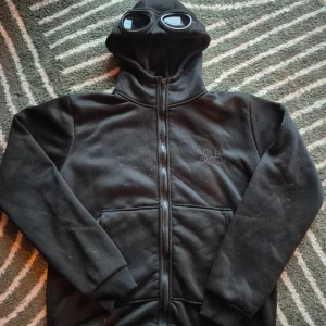  C.P. Company goggles - Svart hoodie från C.P. Company med ikoniska goggles. Skick 8/10
