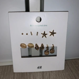 Guldiga örhängen med havstema från H&M - Set med flera par guldiga örhängen från H&M, inspirerade av havet. Innehåller små stjärnor, snäckor, runda hängen och enkla studs. Perfekt för dig som gillar att mixa och matcha olika former och detaljer. 