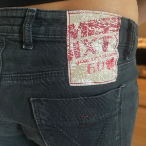 Svarta Miss Sixty bootcut jeans leopard detaljer - Snygga svarta från Miss Sixty med bootcut och låg midja. Byxorna har klassiska fickor, coola röda detaljer och en stor logga bak. Leopard, animal print detaljer. Perfekta för dig som vill ha en retro och trendig vibe, vintage.