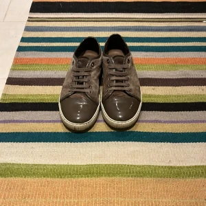 Grå mockasneakers från Lanvin - Snygga sneakers från Lanvin i grå mocka med glansig tå i mörkgrått och matchande snörning. Skorna har en vit sula och diskreta detaljer i lack. Perfekta för dig som gillar stilrena och exklusiva sneakers med en twist. Tvättar innan jag skickar dom, passar 42.