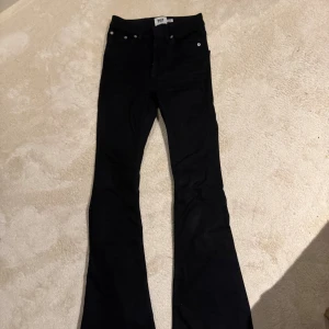 Svarta bootcut jeans från 157 - Svarta jeans från 157 i modellen Sharp Flare. Byxorna har klassisk femficksdesign, dragkedja och knapp framtill samt bootcut-ben som ger en snygg siluett. Perfekta för dig som gillar en stilren look med lite extra edge.
