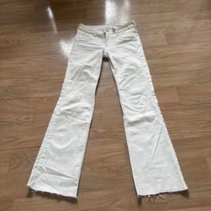 Vita bootcut jeans  - Snygga vita bootcut jeans från Adenim med låg midja. Jeansen har klassisk femficksdesign, råa kanter nertill och är tillverkade i bomull. Perfekta för dig som gillar en retroinspirerad look med lite extra vidd vid benslutet.