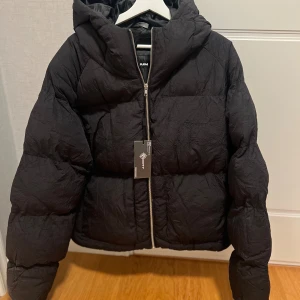 Svart pufferjacka från Vicinity M - Svart pufferjacka från Vicinity i storlek medium. Jackan har en rejäl huva, grov dragkedja framtill och ett stilrent, quiltat mönster. Materialet är syntet och jackan har en loose passform som ger en cool och avslappnad vibe. Perfekt för kalla dagar och streetwear-stil.