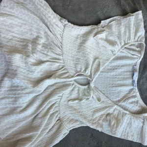 Vit blus från 157 XS - Supersöt vit blus från 157 i storlek XS. Bulsen har kort ärm, knytning framtill och lätt rynkad struktur i tyget. Perfekt för varma dagar med sin luftiga känsla och feminina passform.