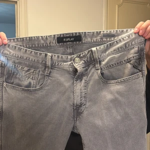 Replay grå jeans slim fit - Snygga grå jeans från Replay med klassisk femficksdesign och diskret Replay-logga på myntfickan. Jeansen har en slim passform och är tillverkade i mjukt denimtyg som ger en skön känsla. Perfekta för dig som gillar stilrena och moderna jeans.