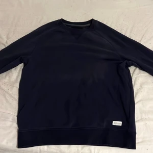 Mörkblå sweatshirt  - En stilren mörkblå sweatshirt från Lager 157 i klassisk modell. Tröjan har rund halsringning, långa ärmar och en liten vit patch nertill. Perfekt för dig som gillar enkel och clean stil. Fråga gärna om mått. Pris kan diskuteras. 