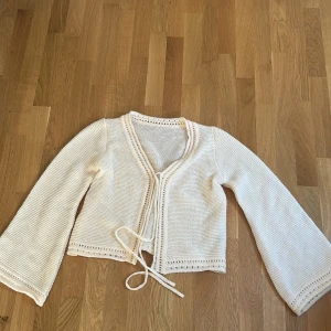 Beige stickad kofta från SHEIN - Supersöt beige stickad kofta från SHEIN med långa trumpetärmar och knytband framtill. Koftan har fina virkade detaljer längs kanterna och är perfekt för lager-på-lager. Mjuk och skön, passar till allt.