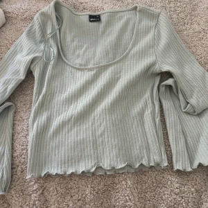 Ljusgrön ribbad topp från Gina Tricot - Supersöt ljusgrön långärmad topp från Gina Tricot i ribbat material. Toppen har en djup, rundad urringning och vågig kant. Kan ej ha så har använts en gång. Tar frakt!