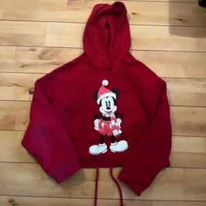 Röd Disney hoodie från Zara, S - Superfin röd hoodie från Zara x Disney med julig Mickey Mouse-tryck framtill. Croppad modell med snörning i midjan och huva. Perfekt för dig som älskar Disney och vill ha en mysig tröja med julkänsla.