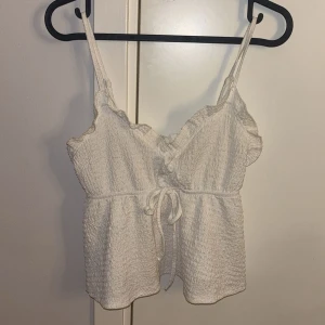 Vit linnetopp med volang - Supersöt vit linnetopp med smala axelband, volangdetaljer längs urringningen och knyt i midjan. Från SHEIN och storlek xs