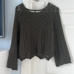 Olivgrön virkad stickad tröja - Olivgrön stickad tröja från only med virkat mönster och vida ärmar. Tröjan har rund halsringning och snyggt vågig nederkant. Perfekt för lager-på-lager och ger en chill boho-vibe till din outfit.