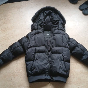 Svart pufferjacket Alessandro Milano - Svart pufferjacka från Alessandro Milano med avtagbar huva och fejkpäls. Är riktigt varm på vintern. Stk s
