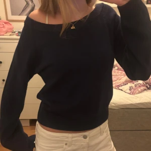 Mörkblå offshoulder stickad tröja - Mysig mörkblå stickad tröja med offshoulder-design och långa ärmar. Tröjan har en avslappnad passform och bred ribbad kant vid midjan och ärmsluten. Perfekt att styla med jeans eller kjol för en chill look.