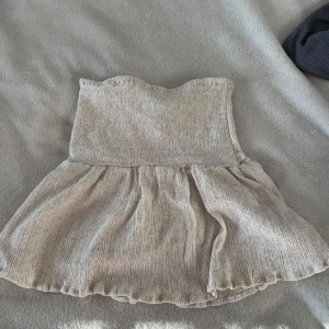Beige kortkjol från ASOS DESIGN - Supersöt beige kortkjol från ASOS DESIGN med smockad midja och lätt volang nedtill. Kjolen är i ett tunt, strukturerat tyg som ger en luftig känsla och passar perfekt till varmare dagar. Enkel att styla med crop tops eller oversized tröjor. Stretchig så den passar mig som är S. 