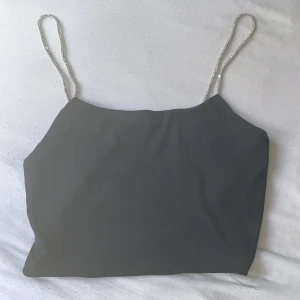 Svart linnetopp med glittriga band - Säljer en svart linnetopp från FB Sister i storlek L. Toppen har tunna axelband täckta av glittrande stenar som ger en extra snygg touch. Enkel och stilren design som passar perfekt till en cool outfit.