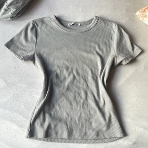 Grå ribbad t-shirt från Zara - Snygg grå ribbad t-shirt från Zara med rund halsringning och korta ärmar. T-shirten har en figurnära passform och är tillverkad i mjuk bomull, perfekt för en clean och stilren look.