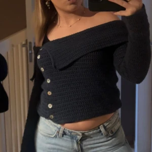 Mörkblå offshoulder kofta från Zara - Säljer en mörkblå stickad kofta från Zara med offshoulder-design och snygga knappar framtill. Koftan är virkad, har lång ärm och en croppad passform som ger en trendig look. Perfekt att styla med jeans eller kjol för en cool vibe.