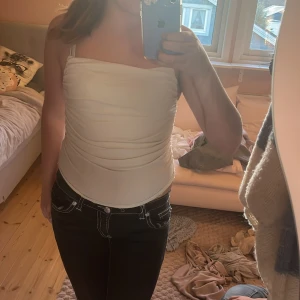 Vit croppad linnetopp med smala band - Säljer en vit croppad linnetopp med smala axelband och lätt rynkad effekt på sidorna. Toppen har en rak halsringning och är figurnära i passformen. Materialet är mjukt och har en lätt struktur som ger en snygg look. Perfekt att styla med jeans eller kjol.