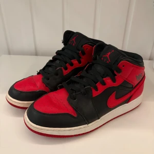 Nike Air Jordan 1 Bred sneakers - Säljer ett par ikoniska Nike Air Jordan 1 i klassiska Bred-färgen. Skorna har svart och rött skinn, svart snörning och röd yttersula. Perfekta för dig som vill sticka ut med en tidlös och sportig look. Mjukt foder och snygga detaljer med Jordan-logga på sidan.
