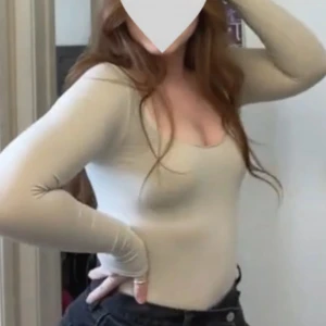 Beige långärmad bodysuit med djup urringning - Säljer en beige långärmad bodysuit med djup, rundad urringning. Toppen är tight och figurnära med slät yta och är tillverkad i ett stretchigt bomullsmaterial. Perfekt att styla med jeans eller kjol för en clean look.