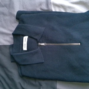 Mörkblå halvzip-tröja Samsoe Samsoe - Mörkblå stickad tröja från Samsoe Samsoe med krage och snygg half zip-dragkedja framtill. Tröjan har lång ärm och är tillverkad i mjukt material som passar perfekt för kyligare dagar. Enkel och stilren design som funkar till det mesta.