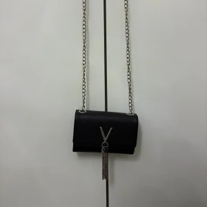 Svart axelväska från Valentino - Snygg svart axelväska från Valentino med kedjerem i silver och ett stort V i metall framtill. Väskan är i präglat skinn och har en stilren, boxig form. Perfekt för dig som vill ha en statementväska med lyxig känsla och coola detaljer. Det går även att ha den som en kuvertväska. B 17 x H 11.5 x D 4 cm. Längd på rem: 17cm. Fri frakt kan jag lösa. 