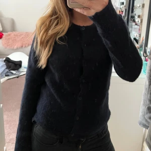 mörk blå kofta från Gina Tricot - Mysig svart kofta från Gina Tricot med rund halsringning och knäppning framtill. Koftan är långärmad och har en fluffig, stickad känsla som passar perfekt till lager-på-lager. Enkel och stilren design som funkar till många outfits.