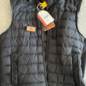 Svart dunväst från Parajumpers - Snygg svart dunväst från Parajumpers med quiltad design och dragkedja framtill. Västen har en gul detalj vid kragen och diskret PJS-logga på bröstet. Perfekt för lager-på-lager och har praktiska fickor på sidorna.