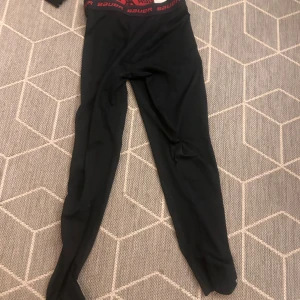 Svarta kompressionstights från Bauer - Svarta kompressionstights från Bauer med röd resår i midjan där det står 'Bauer'. Tightsen är tighta och gjorda i syntetmaterial, perfekta för träning eller sport. Snygg och sportig look med smal passform och stretchig känsla. Går att använda som målvakt jag gjorde det