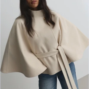 Poncho jacka Nelly - Säljer en beige poncho jacka ifrån Nelly med hög krage och knäppning vid halsen. Jackan har vida ärmar och ett matchande bälte i midjan för snygg siluett. Perfekt för dig som vill ha en stilren och trendig look. Den är slutsåld på Nellys hemsida använd 1 gång