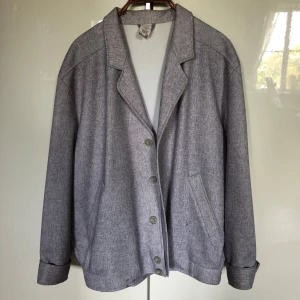 Grå overshirt med knappar - Stilren grå overshirt med klassisk krage och knäppning framtill. Jackan har två snedställda fickor och en avslappnad passform. Materialet är mjukt och lätt, perfekt för lager-på-lager. Ärmarna är långa och kan vikas upp för en mer chill look.