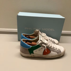 Philippe Model Skor - Stilrena Philippe Model sneakers i vitt skinn med detaljer i grå mocka, grönt, blått och mörk orange. Klassisk låg modell med snörning och rund tå. Philippe Modelsen är inköpta på El Corte Inglés Marbella för 340€. BOX ingår! Skorna har en cool färgblock-design och är tillverkade i Italien 🇮🇹 . Priset ej hugget i sten.  Hör av er vid frågor eller funderingar! 
