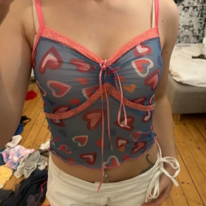 Blå mesh linnetopp med hjärtan - Säljer en blå mesh linnetopp med rosa spetsdetaljer och snörning framtill. jag köpte den från en annan användare på plick, passar xs och är sheer material