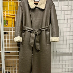 Brun/grön lång pälskappa från ASOS DESIGN - Säljer en lång khaki/brun pälskappa från ASOS DESIGN med fuskpälsfoder på insidan. Jackan har bälte i midjan, uppvikta ärmslut med pälsdetalj och två fickor.  Strl 36- har en oversized passform så passar även för strl 38 (min strl).