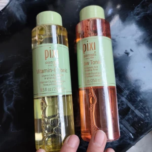 Pixi Vitamin-C & Glow Tonic toner - Två stora flaskor toner från Pixi, Vitamin-C Tonic med gul färg och Glow Tonic med orange färg. Båda har gröna lock och etiketter, innehåller 250 ml och är perfekta för att fräscha upp huden och ge glow. Snygga flaskor som är enkla att använda i din hudvårdsrutin.