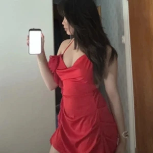 Röd kort klänning med volangdetalj - Säljer en röd kort klänning med tunna axelband och snygg volangdetalj vid bysten. Klänningen har öppen rygg och en draperad effekt framtill som ger en trendig look. Perfekt för dig som vill sticka ut med en färgstark och feminin stil.