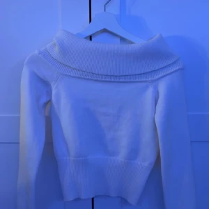 Vit offshoulder stickad tröja - Säljer en vit stickad tröja med bred offshoulder-krage och långa ärmar. Tröjan har ribbad kant vid midjan.
