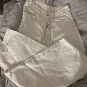 Vita raka jeans  - Säljer ett par vita mid waist jeans med raka ben och klassisk femficksdesign. Byxorna har hög midja och stängs med knapp och dragkedja. Perfekta för dig som vill ha en clean och stilren look.