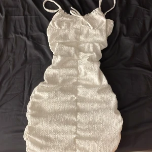 Vit kort klänning från H&M Divided - Supersöt vit kort klänning från H&M Divided med broderade detaljer och smala axelband. Klänningen har knyt framtill och är tillverkad i bomull, perfekt för varma dagar. Snygg passform och lätt material som känns luftigt och fräscht.