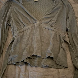 Svart omlottopp med v-ringning - Säljer en svart omlottopp med v-ringning och långa ärmar. Toppen har en lös passform med volangliknande nederdel och markerad midja. Perfekt för dig som gillar en avslappnad men ändå snygg stil.