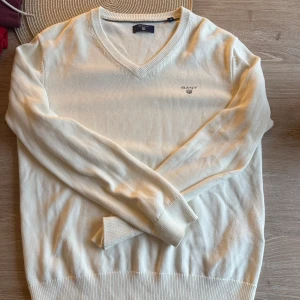 Vit v-ringad tröja från Gant - Klassisk vit v-ringad tröja från Gant med broderad logga på bröstet. Tröjan har långa ärmar och ribbade muddar vid ärmslut och nederkant. Perfekt för en stilren och clean look.