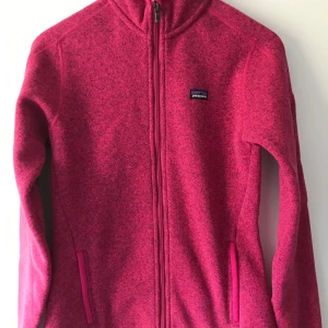 Rosa fleecekofta från Patagonia S - Säljer en snygg rosa fleecekofta från Patagonia i storlek S. Koftan har hel dragkedja framtill, två fickor och en liten logga på bröstet. Tillverkad i mjuk polyester och perfekt för kyliga dagar. Långärmad och riktigt skön att ha på sig.