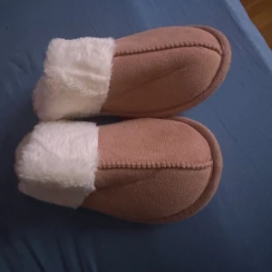 Mysiga skor/tofflor med päls - Supergosiga skor/tofflor i ljusbrunt med fluffig vit päls runt öppningen. Perfekta att glida runt i hemma eller i skolan på jobbet osv när det är kallt. Utsidan är i mjuk mockaliknande syntet och insidan är helfodrad med pälsimitation för extra värme och komfort.