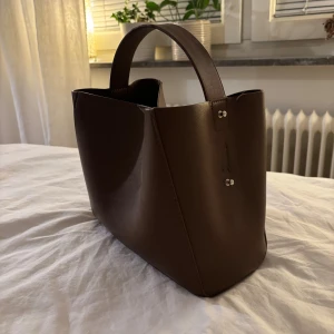Brun handväska - Brun handväska från gina tricot <33 använd en gång. Har gått upp lite vid sidan av handtaget, men inget som syns och kan fixas enkelt!