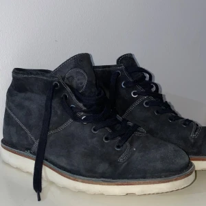 Svarta mockakängor PS by Paul Smith - Svarta kängor från PS by Paul Smith i mjuk mocka med vita gummisulor och svarta snören. Snygga kontrastsömmar och diskret logga på plösen. Perfekta för dig som gillar stilrena och klassiska boots med modern touch.