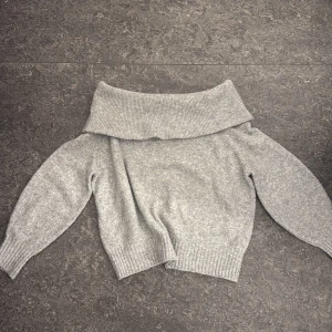 Grå offshoulder stickad tröja H&M - Supermysig grå stickad tröja från H&M med bred offshoulder-krage. Tröjan har lång ärm och ribbade muddar vid ärmslut och nederkant. Perfekt för kyliga dagar när du vill vara både snygg och bekväm.