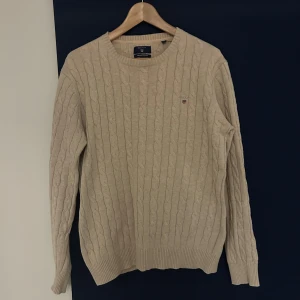 Kabelstickad GANT tröja - Kabelstickad beige GANT tröja. Tröjan är i väldigt fint skick och har inte direkt några tecken på användning.
