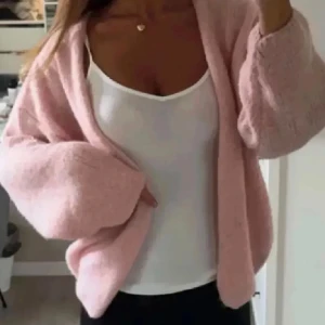 Ljusrosa stickad kofta från Linsery - Supermjuk och fluffig ljusrosa stickad kofta från Linsery. Koftan har en öppen design utan knappar, långa ärmar och en oversized passform. Perfekt att slänga på sig när du vill vara både chill och snygg.